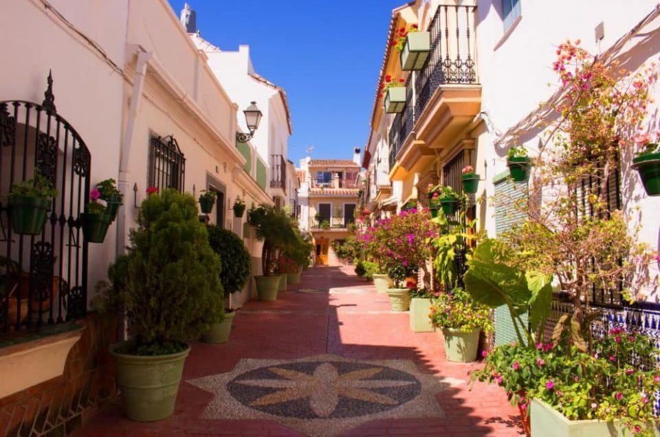 Colorful Mediterranean street lined with vibrant flowers and potted plants in southern Spain.