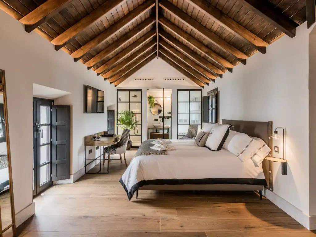 Luxury hotel room in Marbella featuring a wooden vaulted ceiling, stylish decor, and a comfortable b.