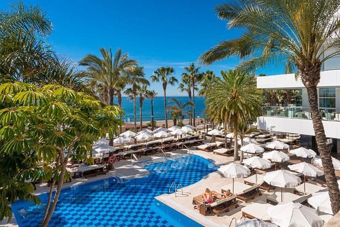 Luxurious hotel pool in Marbella with palm trees and ocean view, perfect for relaxing stays on Costa.