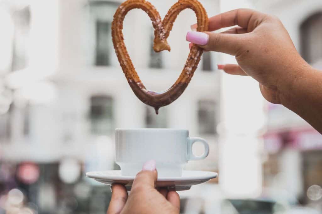 Hand holding a churro shaped like a heart over a coffee cup in Malaga.