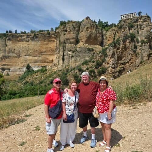 Group of tourists exploring a scenic cliffside with ancient ruins and aqueducts in the background.