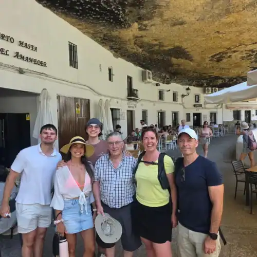 Group of tourists enjoying a guided tour at Costa Excursions under a large rock overhang.