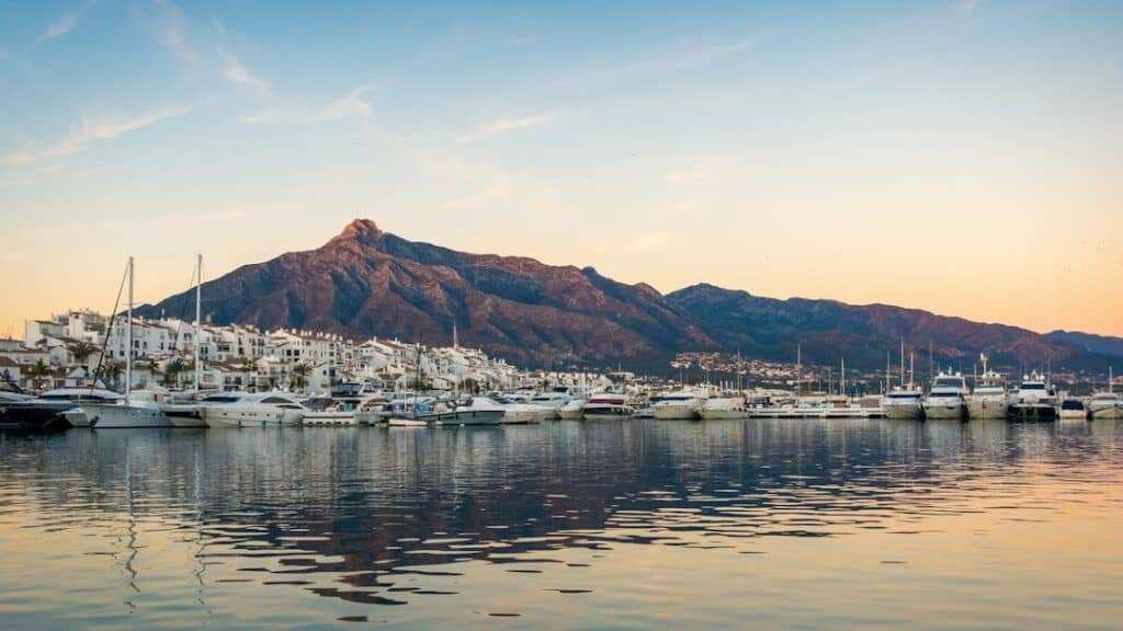 Marbella harbor with yachts and mountain backdrop at sunset.