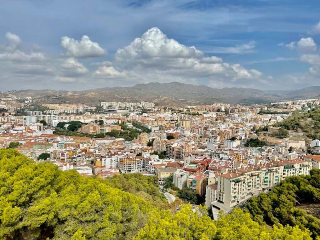 Panoramic view of Malaga city skyline with lush green hills in the foreground.