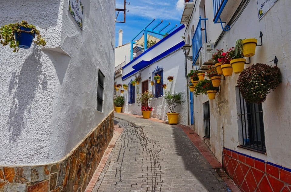 Picturesque narrow street in Andalusia with colorful flower pots and whitewashed walls.