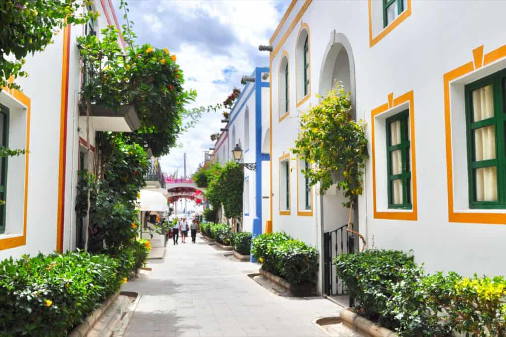 Colorful Mediterranean street with white buildings and vibrant greenery.