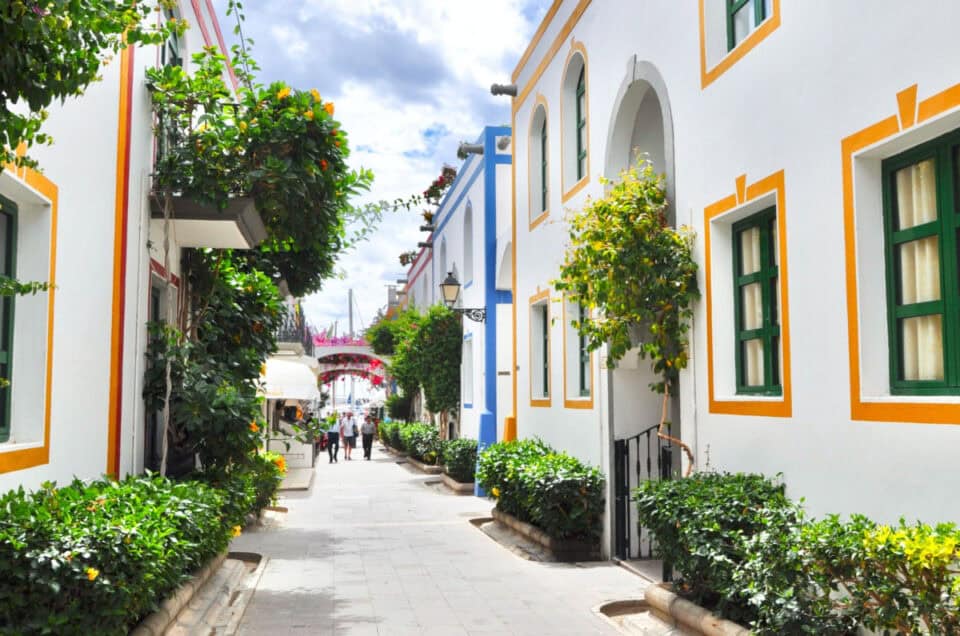 Colorful Mediterranean street with white buildings and vibrant greenery.