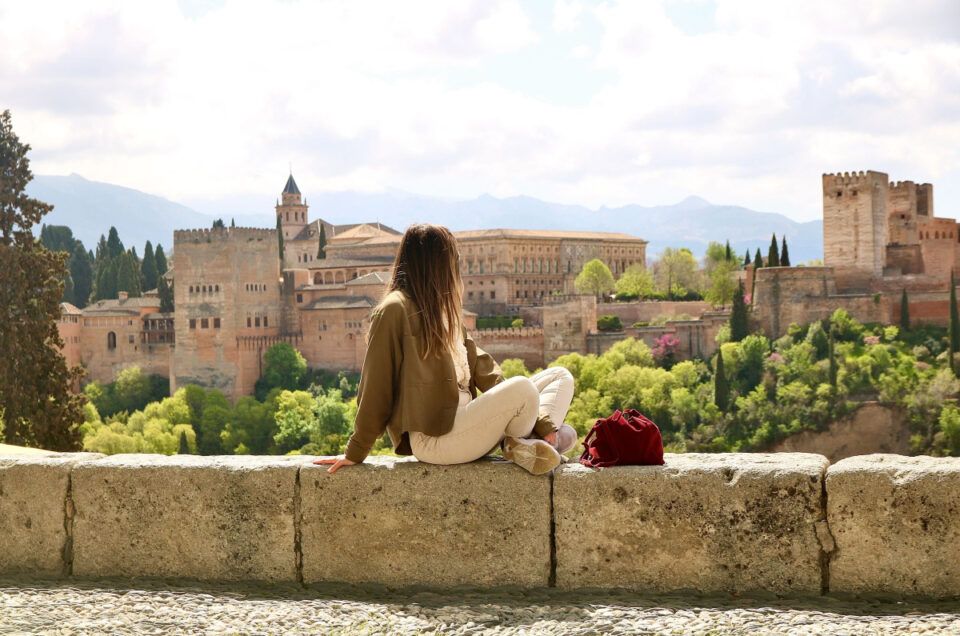 Girl sitting on stone wall overlooking Alcázar of Seville in Spain.
