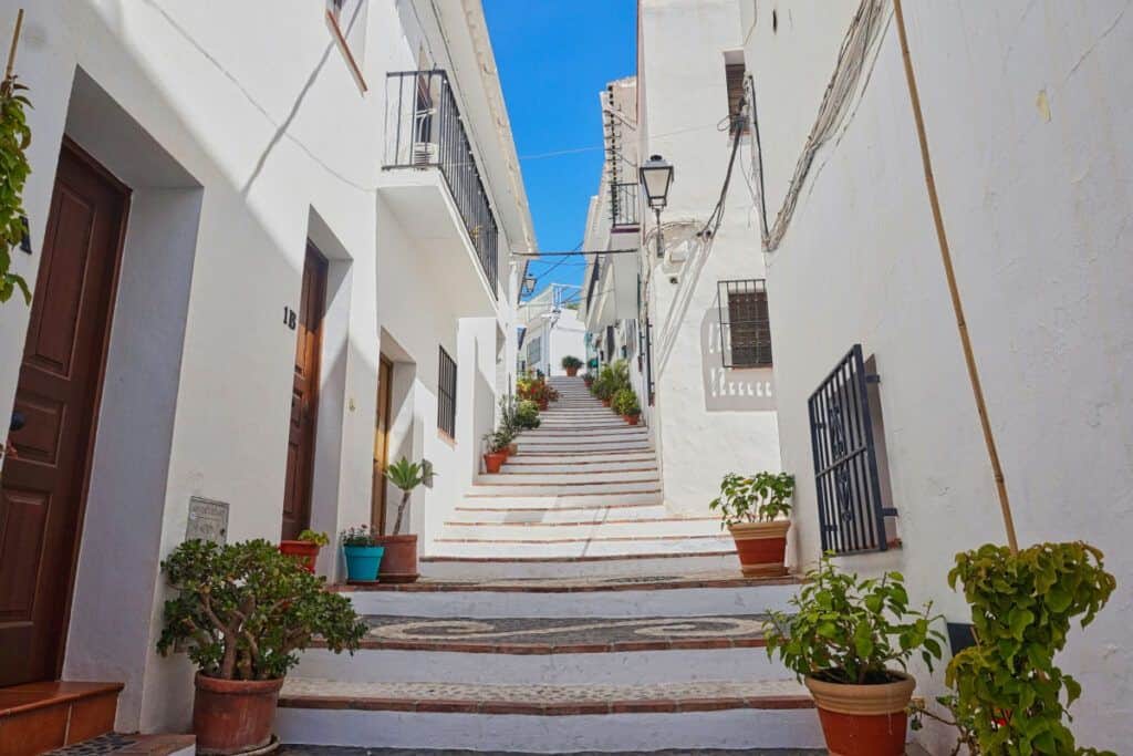 Charming whitewashed street with potted plants and ascending stairs in a Mediterranean village.