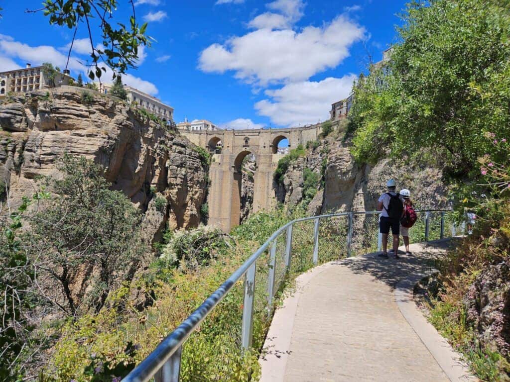 Tourists walking along a scenic path near a historic bridge in Ronda, Spain.